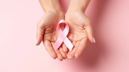Woman's hands holding pink ribbon over pink background. Hope and awareness shot. Support, survivor, prevention. World Breast Cancer Day - Powered by Adobe
