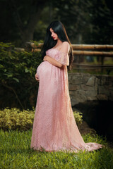 Fototapeta premium Young pregnant woman smiling while standing in an outdoor park surrounded by nature