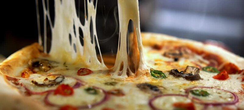Delicious slice of freshly baked pizza with melted mozzarella cheese stretching as it's lifted from the whole pie. The steamy, hot pizza features mushrooms, onions, and spicy peppers