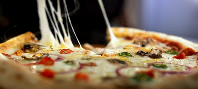 Hot, steaming slice of delicious italian pizza being lifted up, showing long strings of melted mozzarella cheese in an appetizing close-up view from a professional kitchen or restaurant