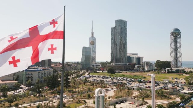 Aerial view pole with georgian national flag waving in Batumi. Georgia modern waterfront with Alphabetic Tower, Technological University Tower, Ferris wheel and Black Sea promenade in summer season