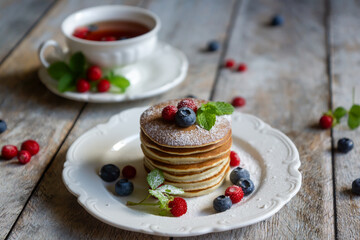 Delicate pancakes with fruits and berries on a wooden table.