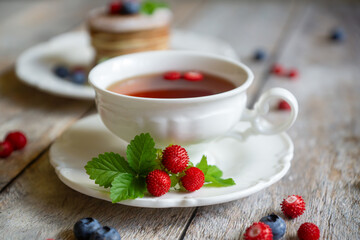Delicate pancakes with fruits and berries on a wooden table.