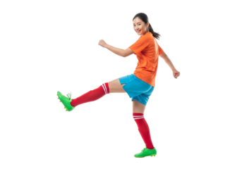 Young woman in orange jersey and blue shorts kicking a soccer ball, isolated on transparent background