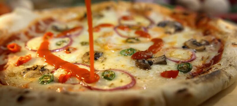 Vertical video of delicious hot pizza with mozzarella cheese, mushrooms, and spicy peppers receiving a final touch as red tomato ketchup is poured in a spiral pattern before serving in a restaurant