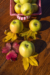 Fresh yellow apples in a wicker basket, arranged on a wooden surface with colorful autumn leaves, perfect for harvest season and organic farming.