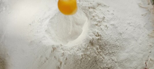 Slow motion of a raw egg falling into a well in a pile of flour on a rustic kitchen table, showing the process of preparing dough for baking homemade bread or pasta from scratch - Powered by Adobe