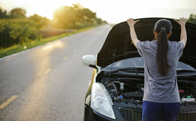 woman driver is standing with the hood open to inspect a broken-down car parked on the side of the road. Car repair and maintenance concepts