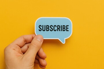 A human hand holds a light blue speech bubble with the word "SUBSCRIBE" in bold black text against a bright yellow background. This image is an example of a simple, modern design.
