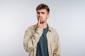 Young man gesturing for silence while thinking in a simple indoor setting during daylight hours