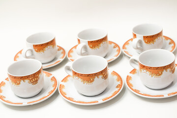 Elegant porcelain espresso cups and saucers with intricate gold detailing on a clean white background