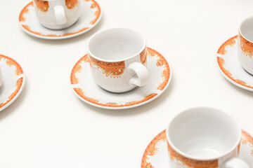 Elegant coffee cups and saucers with intricate orange patterns on a clean white surface
