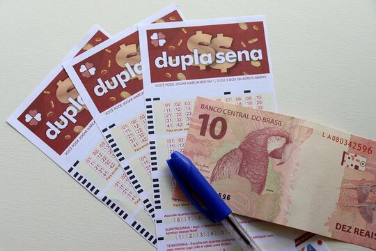 Salvador, Brazil - October 4th, 2025: Dupla Sena game and Brazilian Real banknotes. Brazilian Lottery (Loterias Caixa) concept. Millionaire prize.