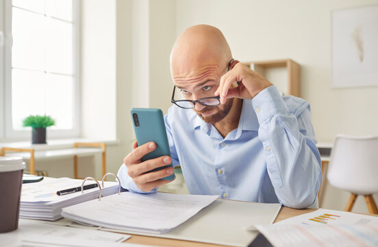 Serious businessman working with phone in office, reading news on a smartphone. Professionals busy schedule, balancing business tasks with staying updated and online on current events.