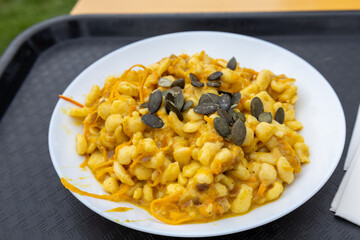 Close-up of a traditional German and Austrian dish, pumpkin spätzle, served with a creamy pumpkin sauce and garnished with roasted seeds. 