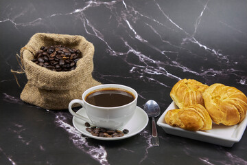 Cup of coffee, close-up, with freshly roasted beans and a croissant to enjoy, copy space and foreground photo.