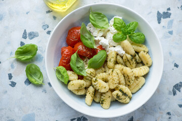 Plate of italian gnocchi with roasted tomatoes, ricotta cheese and green basil, horizontal shot on a white and blue granite background, high angle view