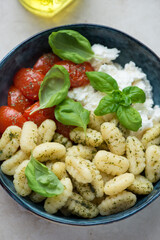 Potato gnocchi with basil oil, ricotta, roasted tomatoes and fresh basil served in a blue bowl, vertical shot, middle closeup