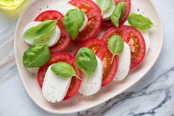 Classic caprese with slices of mozzarella, red tomatoes and green basil leaves on a beige plate, horizontal shot, middle closeup