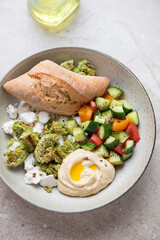 Plate with falafel, hummus, goat cheese and vegetables, vertical shot on a beige stone background, middle close-up
