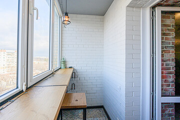 Fototapeta premium A cozy balcony with white brick walls, a wooden countertop by the window, and a hanging light