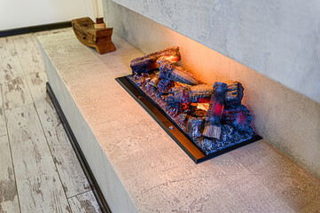 A modern electric fireplace with simulated logs and glowing embers set on a stone mantel. A decorative wooden piece sits nearby