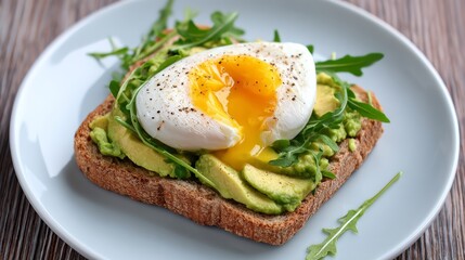 A plate of whole grain toast topped with smashed avocado, arugula, and a perfectly poached egg with a runny yolk