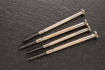 Set of steel screwdrivers for precision mechanics on slate stone, macro, top view.