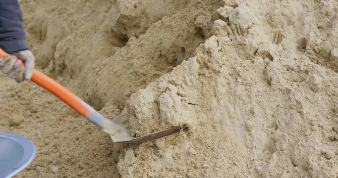 Close up of a shovel in action. Loading sand into a wheelbarrow. Construction excavation work. Slow-motion video in 4K quality