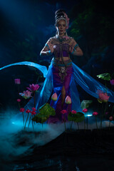 Fototapeta premium Elegant woman in traditional Southeast Asian costume dancing gracefully among lotus flowers
