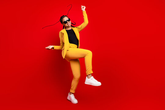 Young elegant woman in a yellow suit enthusiastically expressing joy and energy, posing actively against a vibrant red background
