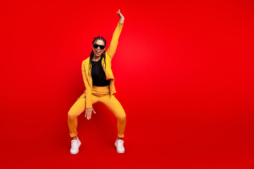 Stylish young woman in a vibrant yellow suit posing on a bold red background, embracing energy and fashionable confidence