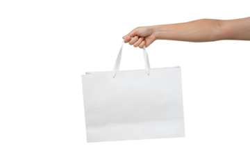 A person's hand holding a paper shopping bag with handles on a clean white background. Studio shot with ample copy space for text, logos, or branding. Isolated on white, cut out.