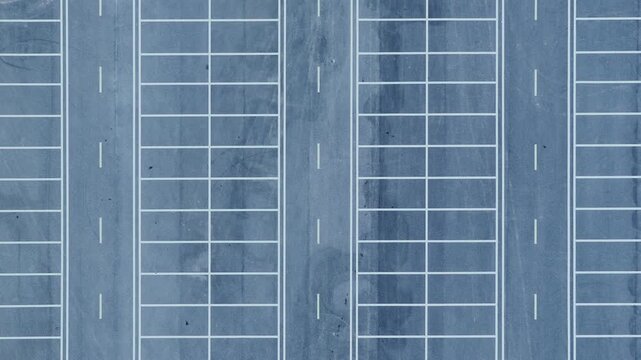 Aerial shot of an empty parking lot with white painted lines creating a minimalist geometric pattern on the blue asphalt.