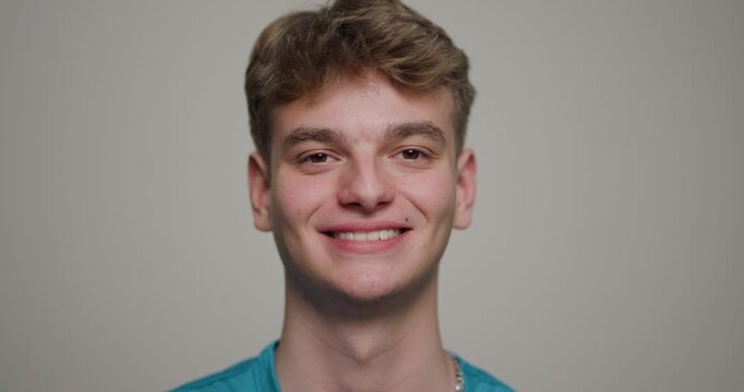 Young man pauses thoughtfully while gazing directly at the camera in a neutral setting, showcasing a confident expression and casual attire
