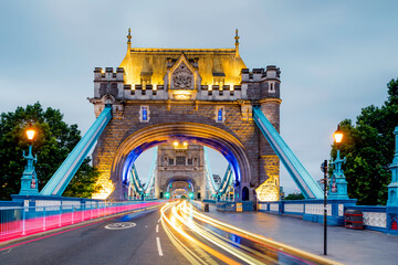 A vibrant long-exposure view of Tower Bridge captures the energy of London in motion. Golden lights illuminate the historic structure as streaks of traffic create a dynamic flow of colour