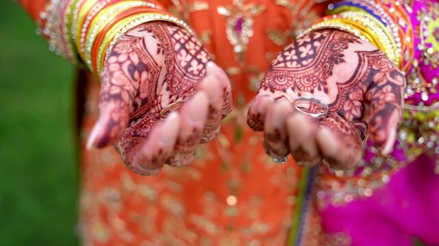 Close up view of Traditional Indian or Pakistan henna painted bridal hand. Colorful clothes, henna tattoo. Bride opens palms showing bride and groom wedding rings.