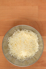 A stainless steel bowl filled with a mound of finely grated Parmesan cheese, rests on a light wooden cutting board