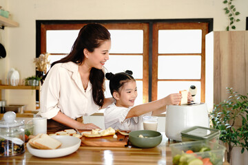 happy Mother teaching daughter making breakfast toast bread with toaster at home kitchen together ....