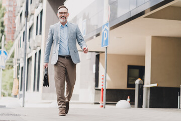 Fototapeta premium Businessman walking in the city smiling carrying briefcase in a modern urban street scene
