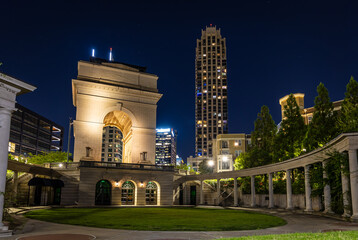Illuminated arch monument in Atlanta at night with city buildings in background