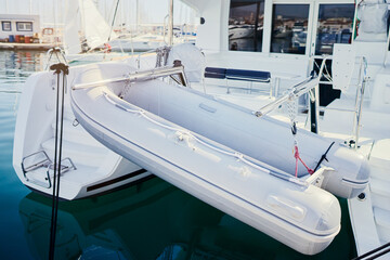 A white inflatable boat is attached to the back of a larger yacht, floating on calm water in a...