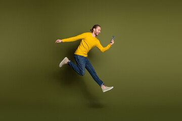 Young man leaping joyfully with smartphone in hand, expressing happiness and style against a green...