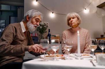 A thoughtful moment shared by a mature couple at a candlelit dinner in a cozy setting.
