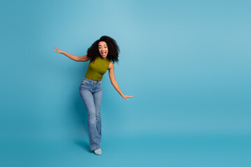 Young woman in a green top and blue jeans posing joyfully on a bright blue background representing vibrant energy