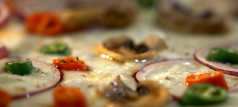 Pizza topped with sliced red onion, green and red bell peppers and mushrooms on mozzarella baking in the oven, close-up showing fresh ingredients and gooey cheese - Powered by Adobe
