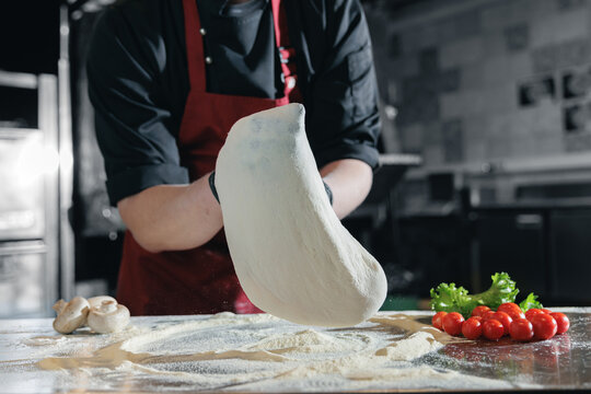 Flying thin Pizza dough preparation by male chef in italian pizzeria kitchen - Powered by Adobe