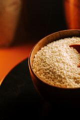 Uncooked couscous in a wooden bowl on a dark surface with soft warm lighting