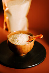 Couscous in a wooden bowl with a wooden scoop placed on a dark surface next to a bag