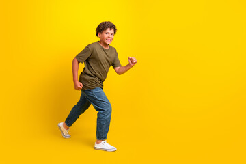 Funny energetic boy runs on bright yellow background wearing khaki green tshirt jeans for playful fitness and fashion vibe